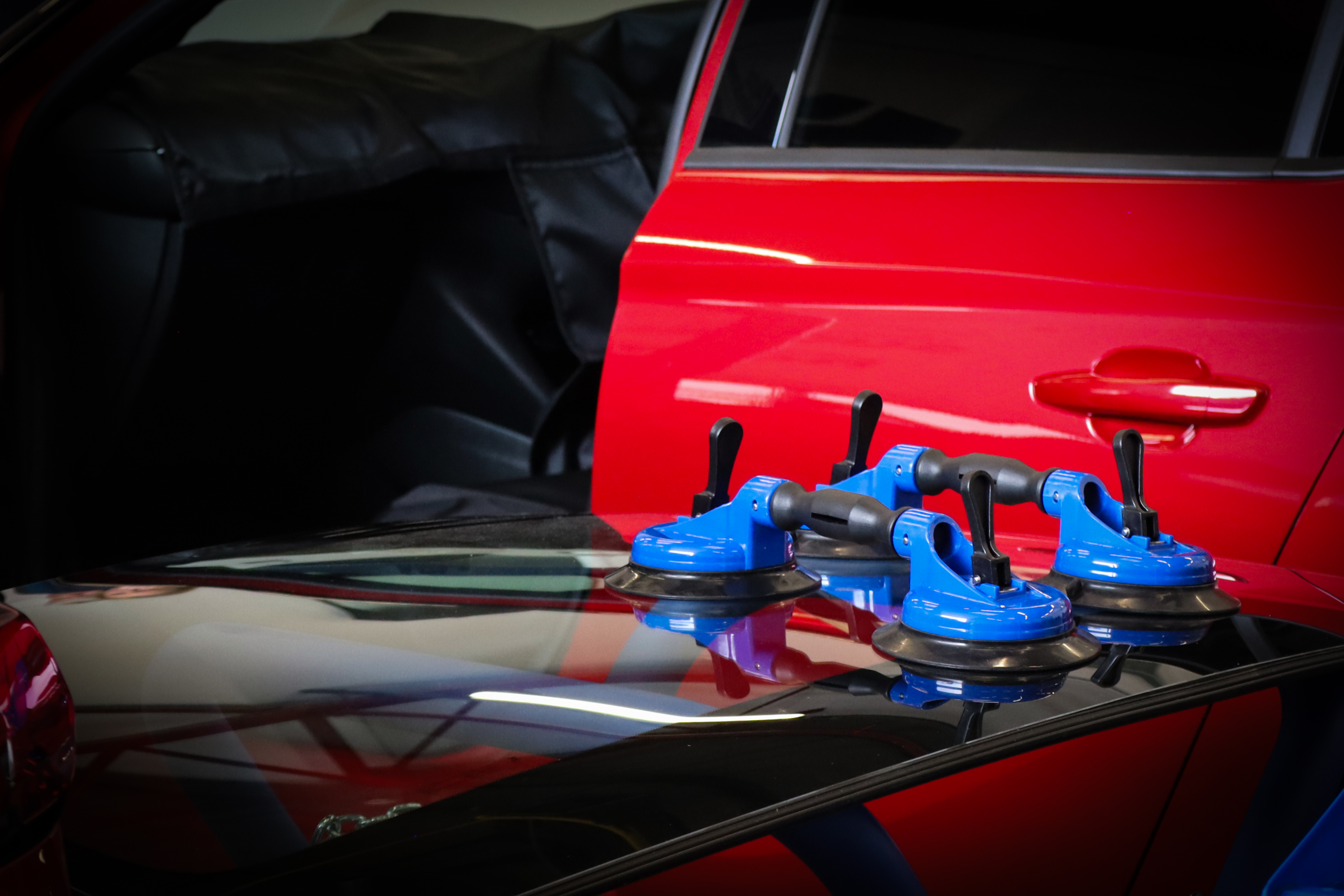 Windscreen on a stand with suction cups on  he surface with a red car door behind.